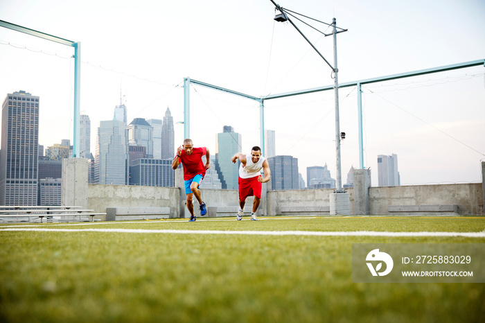 Two men running in sport field cityscape in background