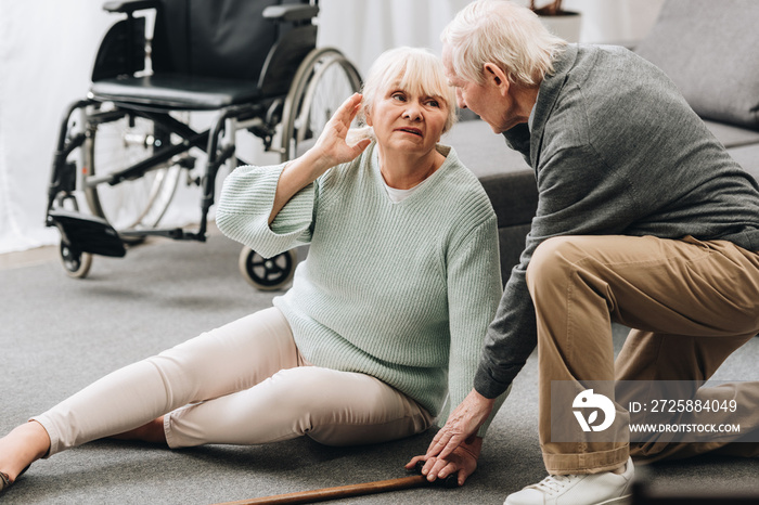 supportive retired husband looking at senior wife sitting on floor