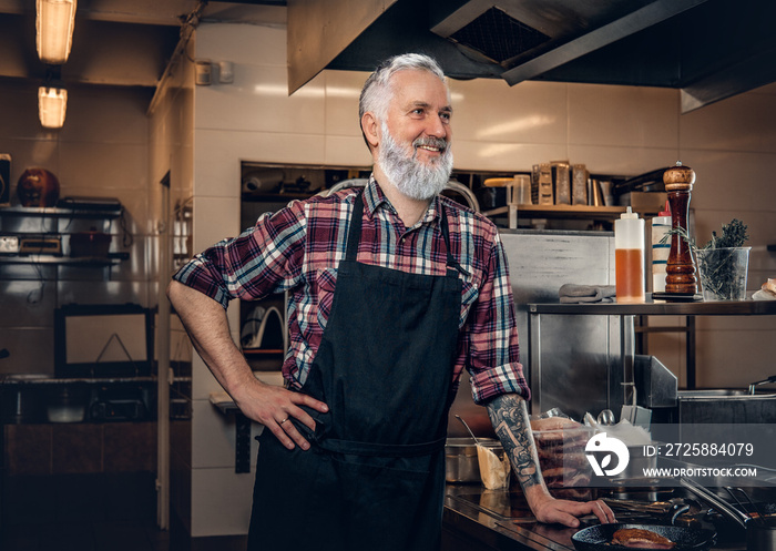 Professional elderly butcher inside modern kitchen of restaurant