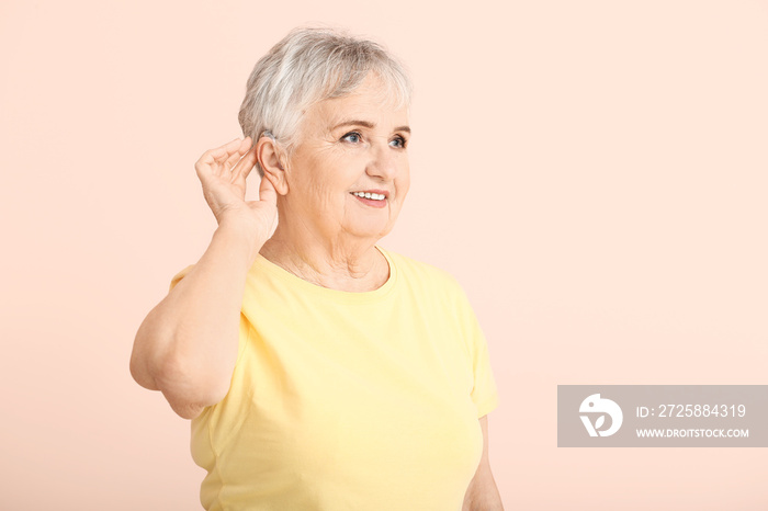 Senior woman with hearing aid on color background