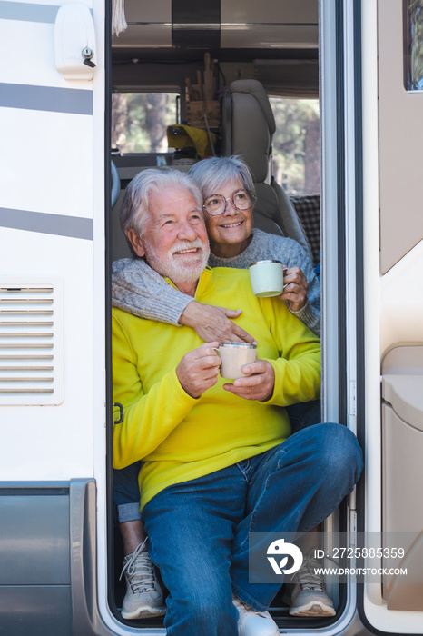 快乐放松的高加索高级夫妇坐在露营车房车的门上，手里拿着咖啡