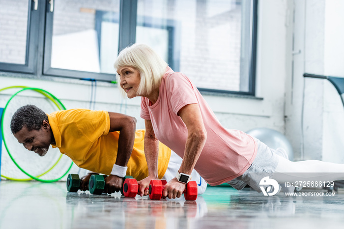 interracial mature couple doing push ups with dumbbells at gym