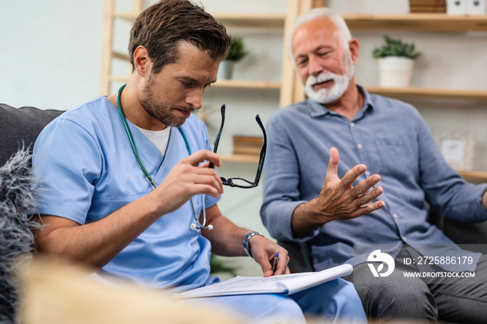 General practitioner analyzing medical documents of senior patient while being in home visit.