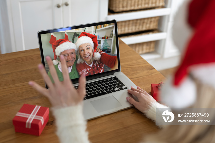 Rear view of woman in santa hat waving while having a videocall with senior couple in santa hats on