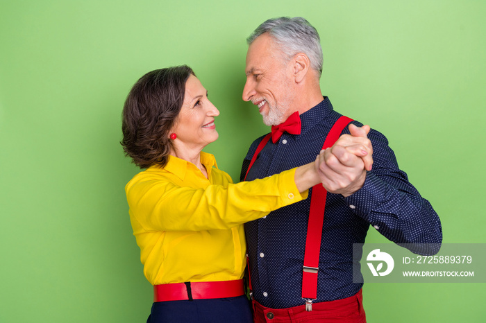 Portrait of two peaceful partners hold hands enjoy event dancing 60s isolated on green color backgro