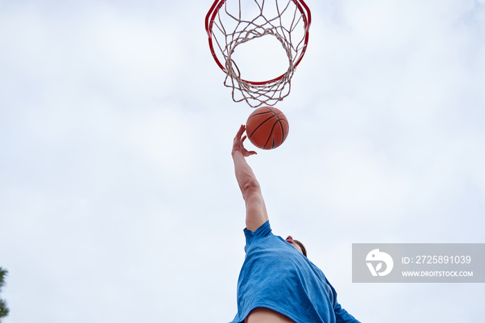 young Caucasian man dunking on an outdoor basketball court. concept of sport