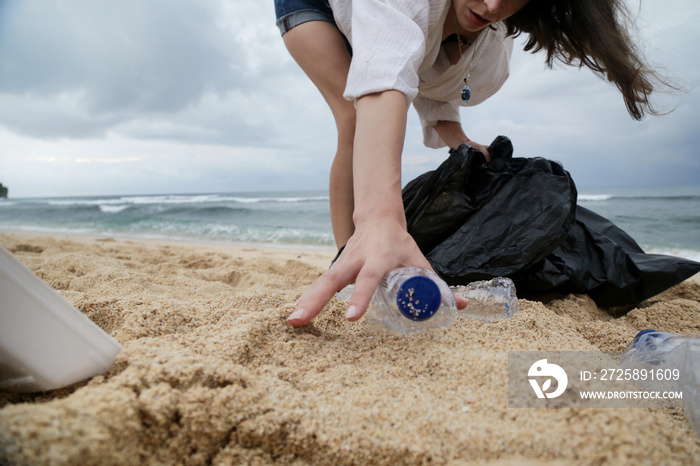 Volunteer woman collecting trash on the beach. Trash-free seas concept. Single-use plastic is a huma