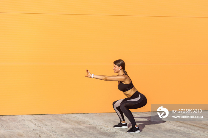 Young attractive woman practicing fitness, doing bodyweight squat exercise, yoga chair pose, working