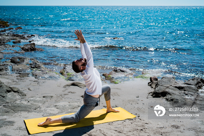 Athletic Caucasian man doing yoga exercises near a sea.