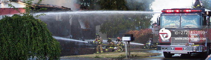 A residential home burns in a house fire as firefighters spay water from a hose in an effort to put 