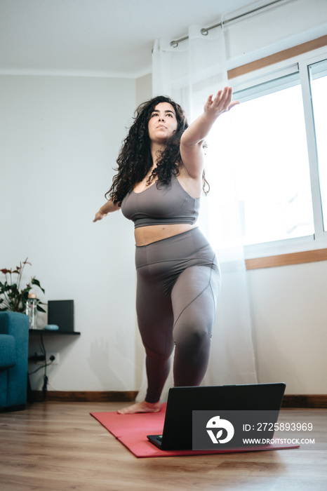 Full length shot of young plus size woman in sportswear doing yoga positions on the floor with a lap
