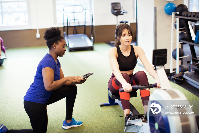 High angle view of instructor using tablet computer while guiding athlete exercising on rowing machi