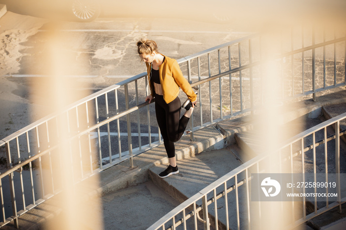 High angle view of female athlete stretching leg while standing on steps seen through railing