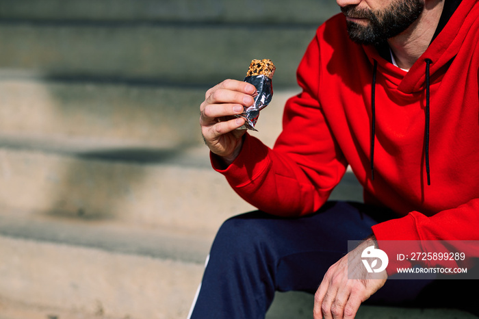 Close-up of runner sitting on the stairs and eating energy bar after running.