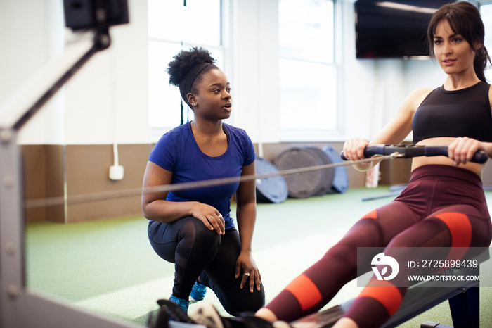 Instructor guiding female athlete exercising on rowing machine in gym