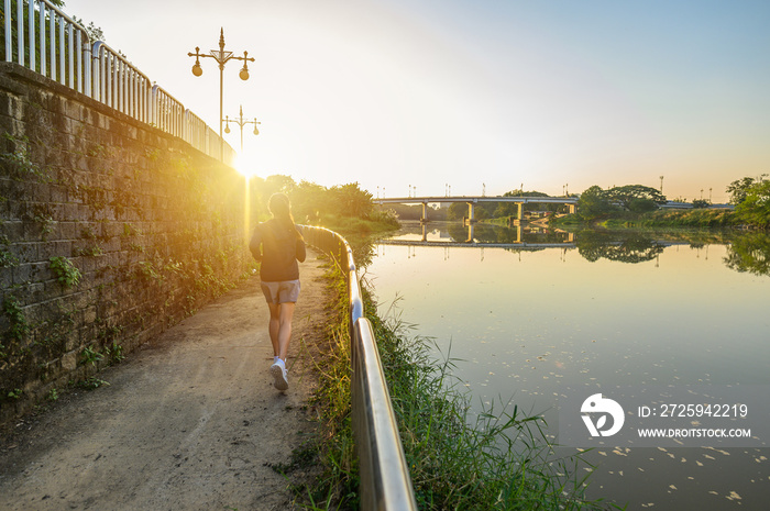 Back view of young fitness woman running at the waterfront with Kok river the river that runs throug