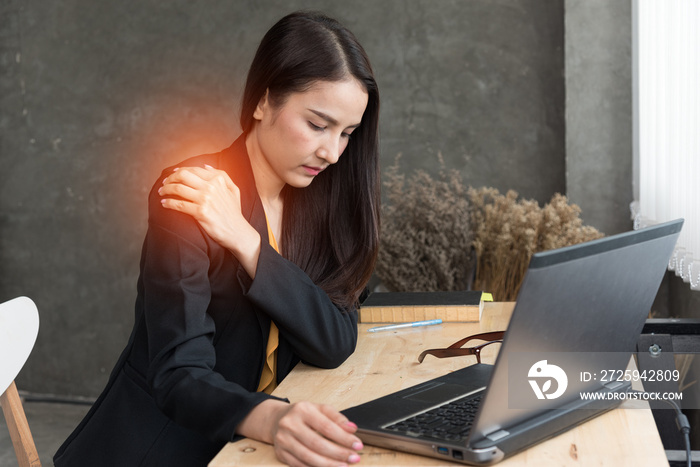 年轻办公室女性坐在办公桌前肩膀疼痛的图像，概念办公室综合征。