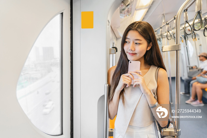 年轻的亚洲女性乘客在地铁列车上通过智能手机使用社交网络