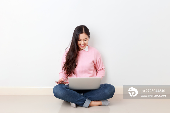 Young attractive collage student sitting by the wall learning online at home, Asian woman using comp