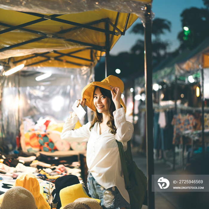 年轻的亚洲成年女性在夜市买黄色帽子。