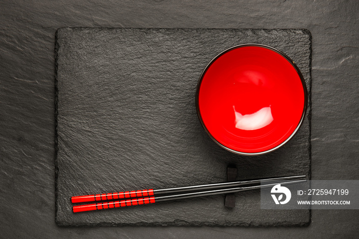 黑色石头背景上的两只筷子和红色盘子，带复制空间，俯视图