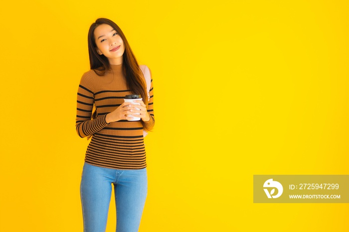 黄色背景下，一位年轻的亚洲美女，手里拿着书包和咖啡杯