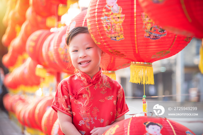 穿着中国传统服装的亚洲小女孩提着红灯笼站在那里，用中文微笑