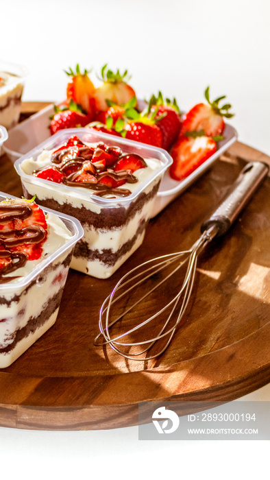 Bolos de pote caseiros sobre mesa de madeira com cobertura de chocolate e morangos.