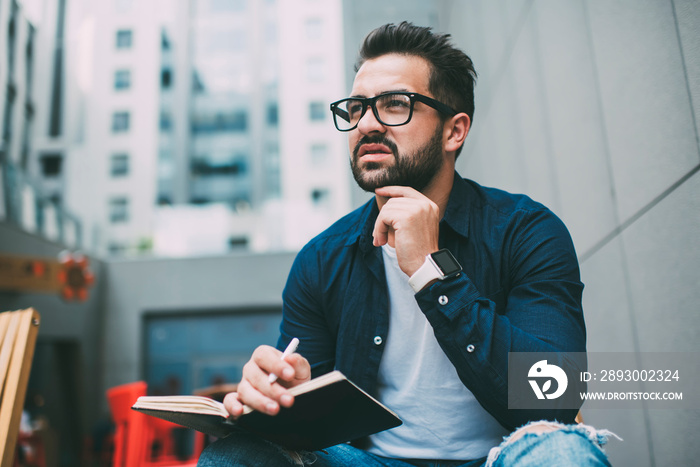 Pensive hipster guy in optical spectacles for vision correction thoughtful looking away spending tim