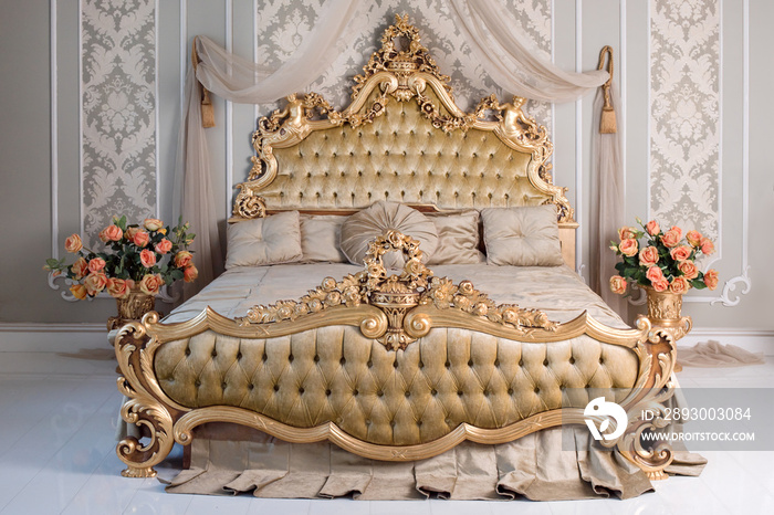 Luxury bedroom in light colors with golden furniture details. Big comfortable double royal bed in el