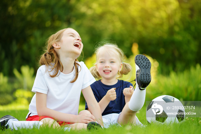 Two cute little sisters having fun playing a soccer game on sunny summer day. Sport activities for c