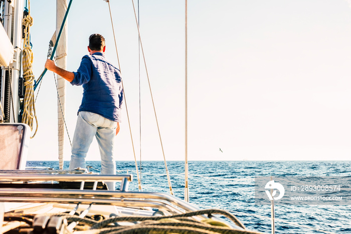 Sailing activity people - man viewed from back stand up on the deck of a sail boat looking horizon a