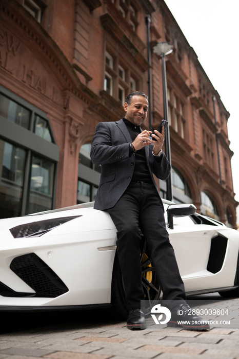 Mature man leaning against luxury car and using phone