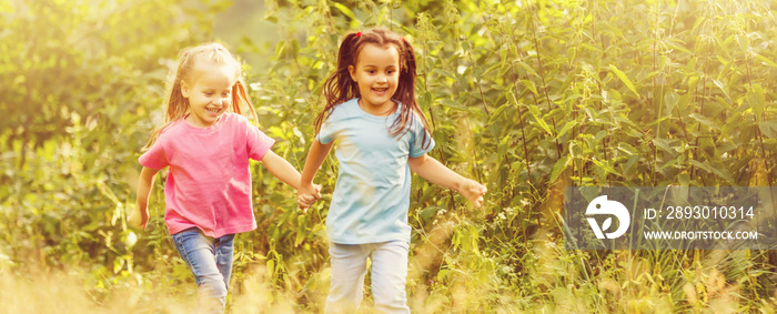 Two little sisters holding each other hands and running forward by the forest road at the sunset