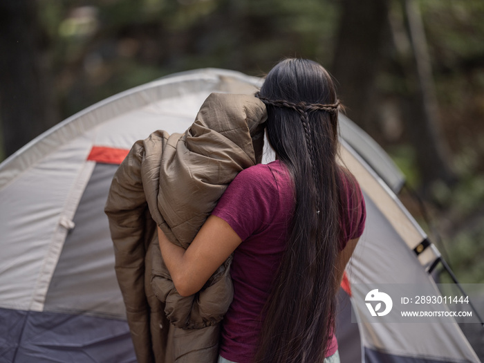 一名土著妇女在露营时把一个睡懒觉放在帐篷里的水平后视图