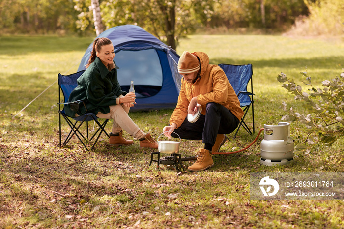 露营、旅游和旅行理念-快乐的情侣在游客身上喝啤酒和煮食物