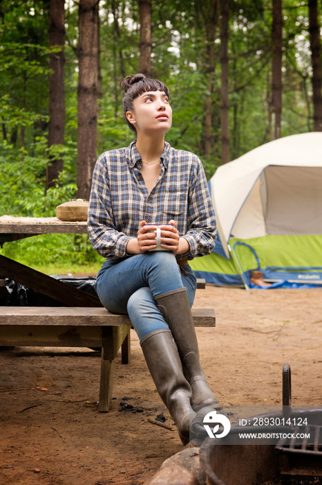 Young woman with coffee cup sitting on bench in forest