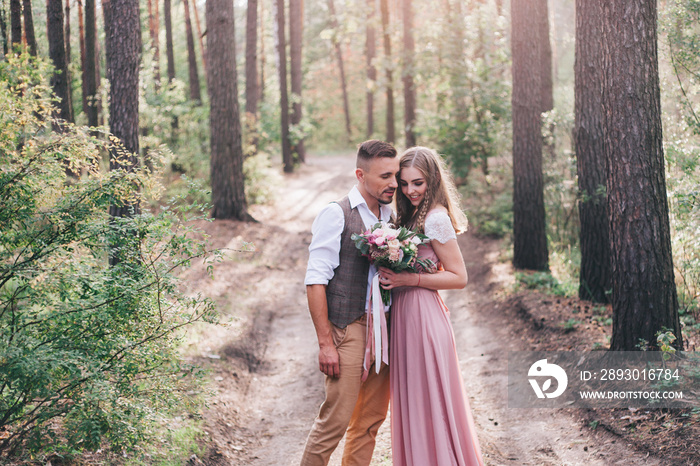 Beautiful couple at the photoshoot of love story in the forest in a rustic dress