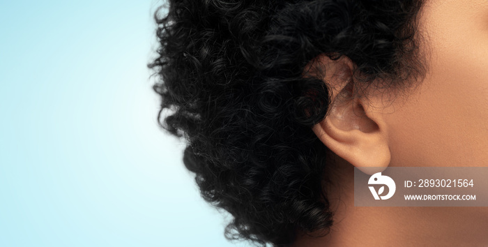 hearing, health and beauty concept - close up of african american womans ear over blue background