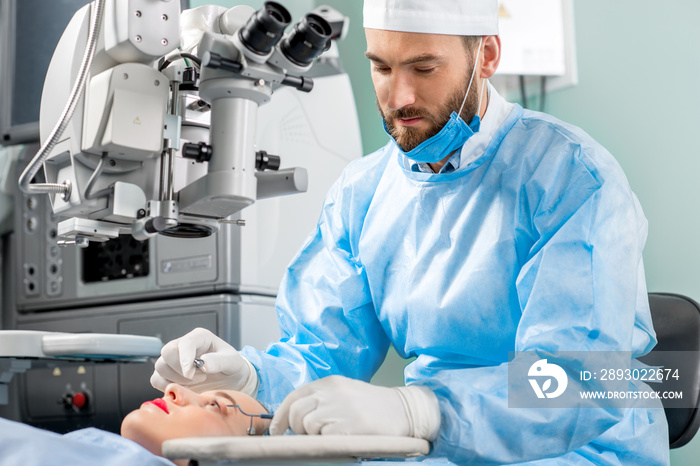 Surgeon operating eye of female patient using surgical microscope at the operating room