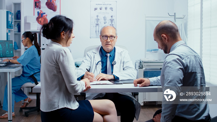 Young couple talking with senior doctor in modern private clinic. Family planning specialist. People