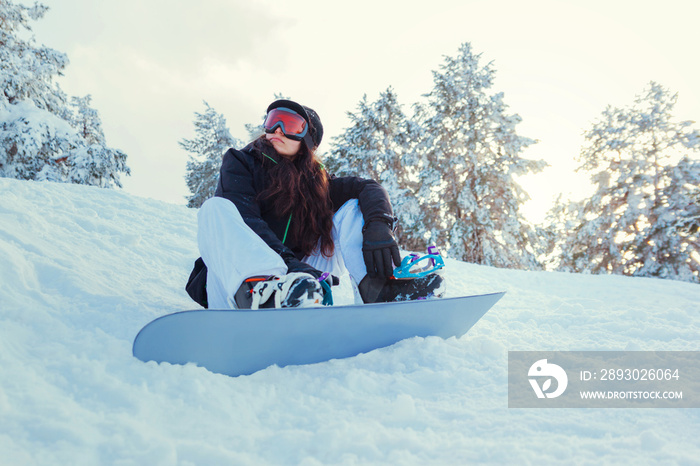 Stock photo of a young woman snowboarder sitting on the snow