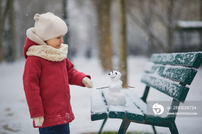 可爱的蹒跚学步的女孩在大雪天堆雪人