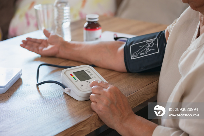 Senior woman is checking blood pressure and heart rate with digital pressure gauge by herself at hom