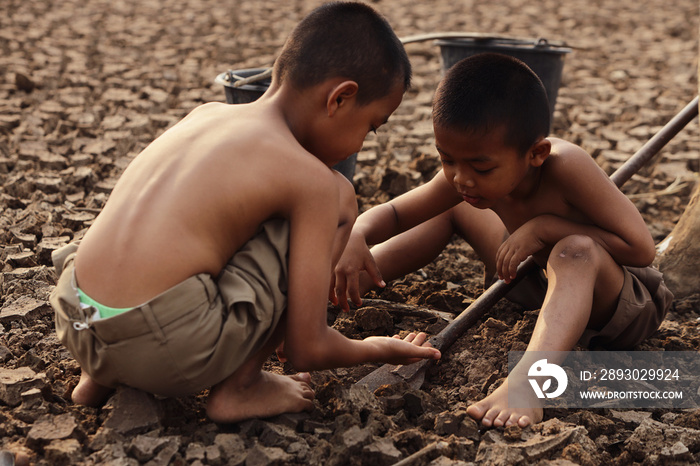 The boy in the wilderness is digging the cracked soil to find food. Global warming and climate chang