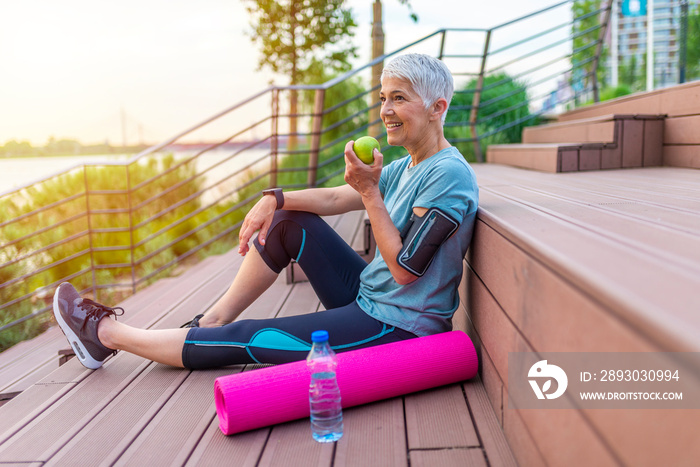 Senior woman eating apple after exercise. Happy mature woman holding green apple while seating at th