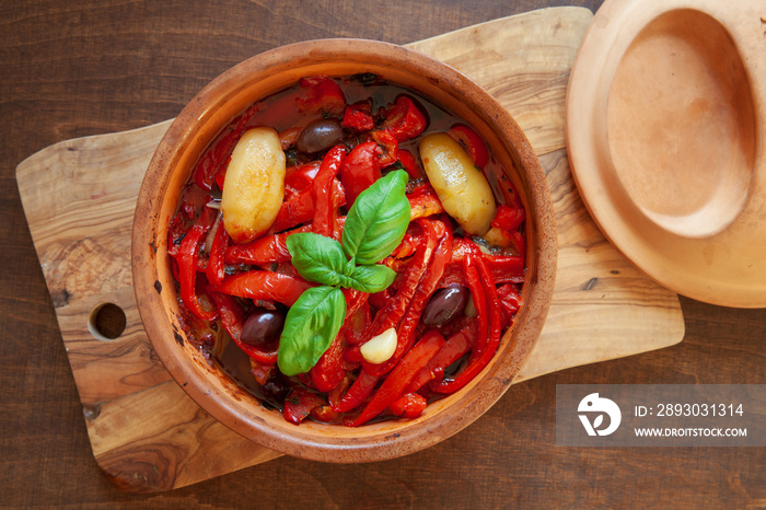 Roasted bell peppers with potatoes, olives, garlic, basil leaves and tomato sauce in clay pot. Itali