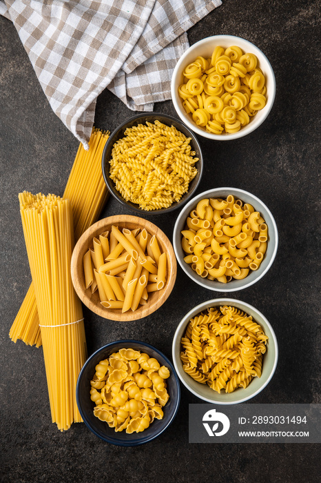 Various types of raw italian pasta in bowls.