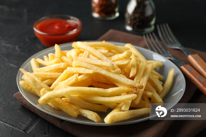 Plate of french fries, napkin, red sauce, forks on black background, space for text. Closeup