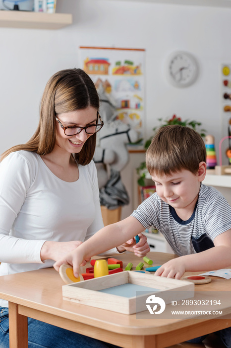 Mother or preschool teacher with cute child playing - education